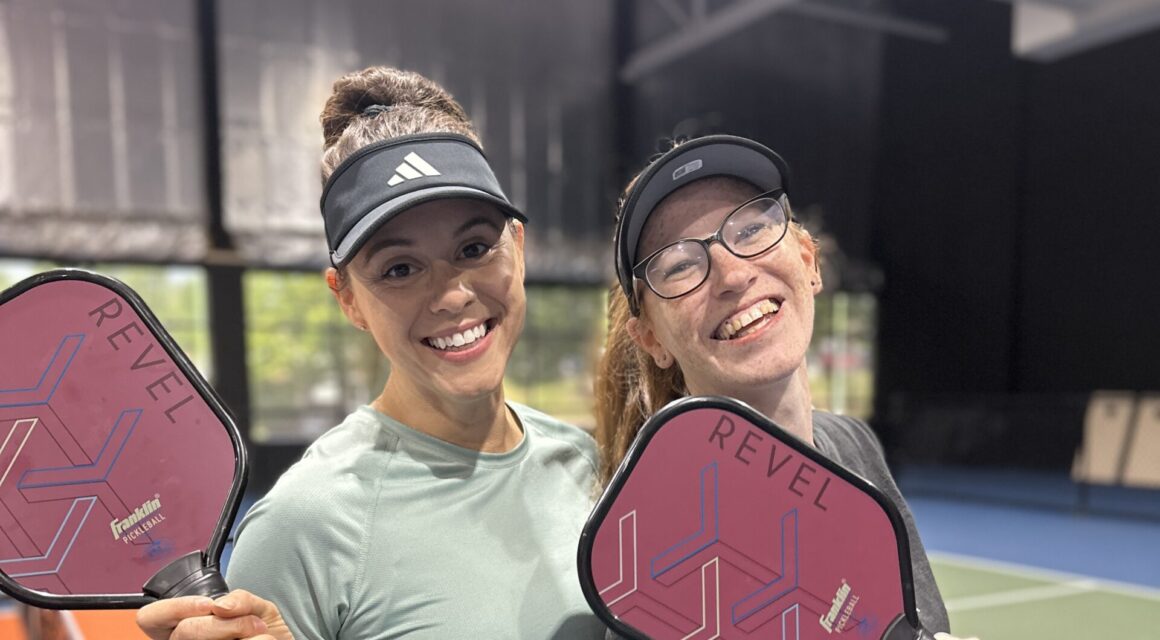 Two women taking a picture with their pickleball paddles